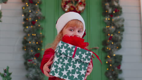 Happy-toddler-child-girl-kid-in-red-sweater-presenting-one-Christmas-gift-box,-stretches-out-hands