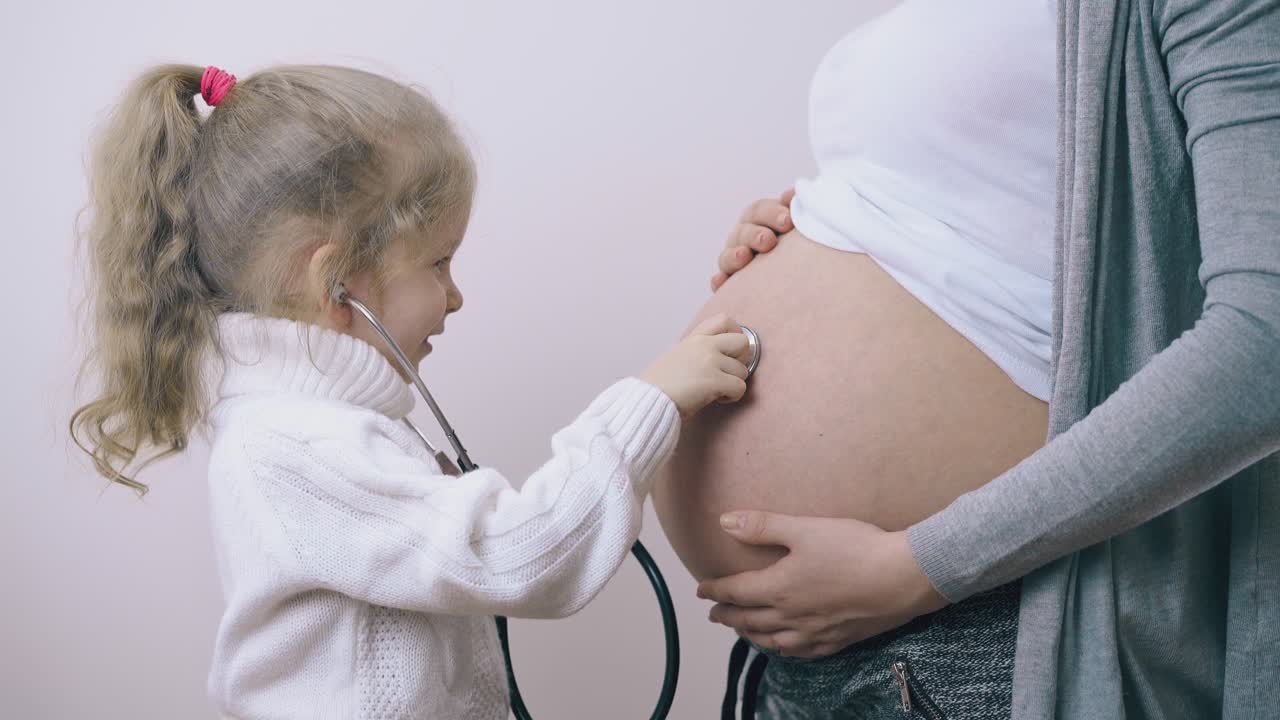 un bambino tocca la pancia di una madre incinta con uno stetoscopio