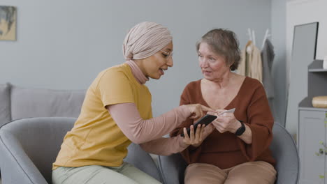 arabic woman teaching an elderly woman to use mobile payment with credit card 1