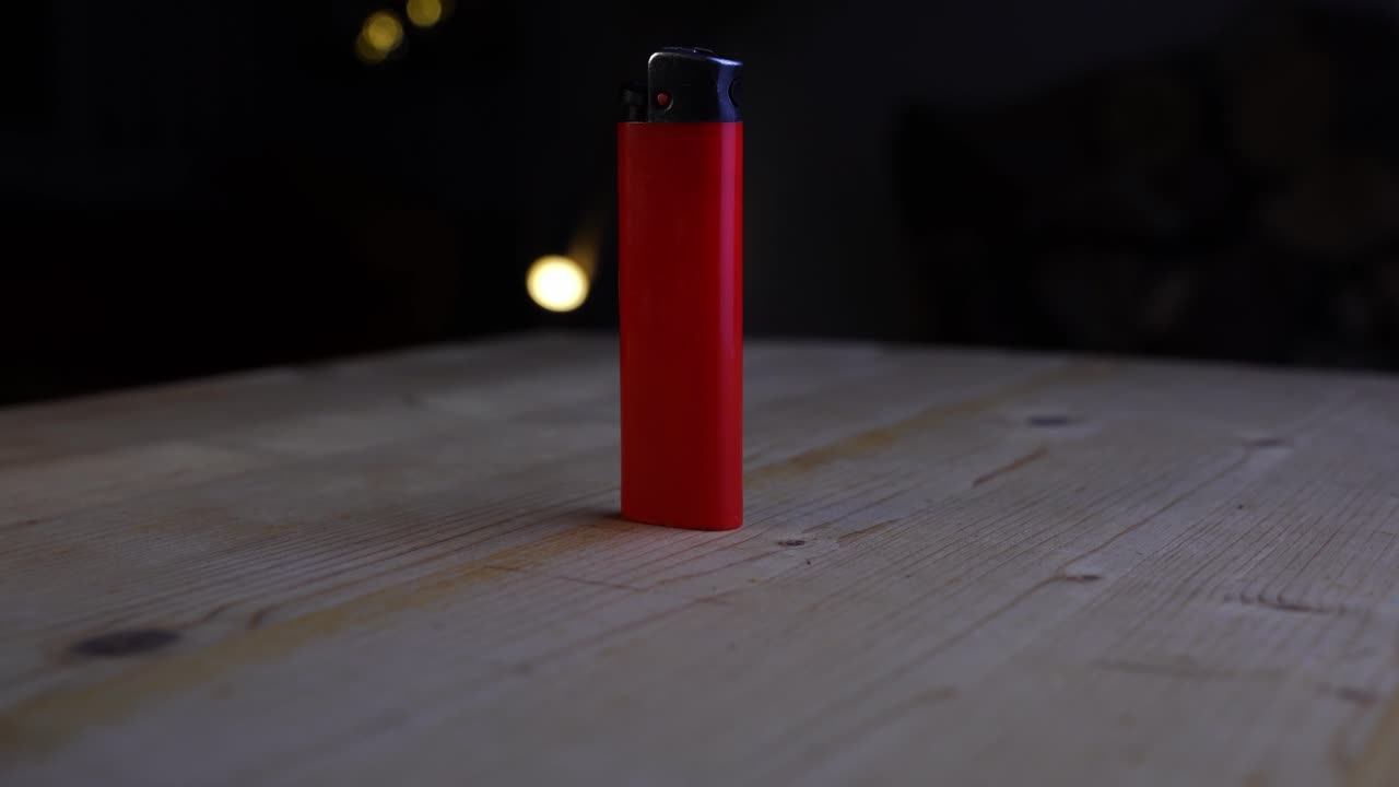 красная зажигалка на темном фоне с несколькими огнями на заднем плане на деревянном столе