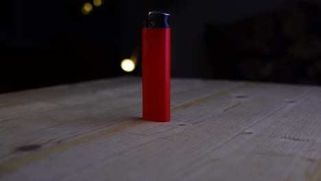 Encendedor-Rojo-Contra-Un-Fondo-Oscuro-Con-Algunas-Luces-En-El-Fondo-Sobre-Una-Mesa-De-Madera