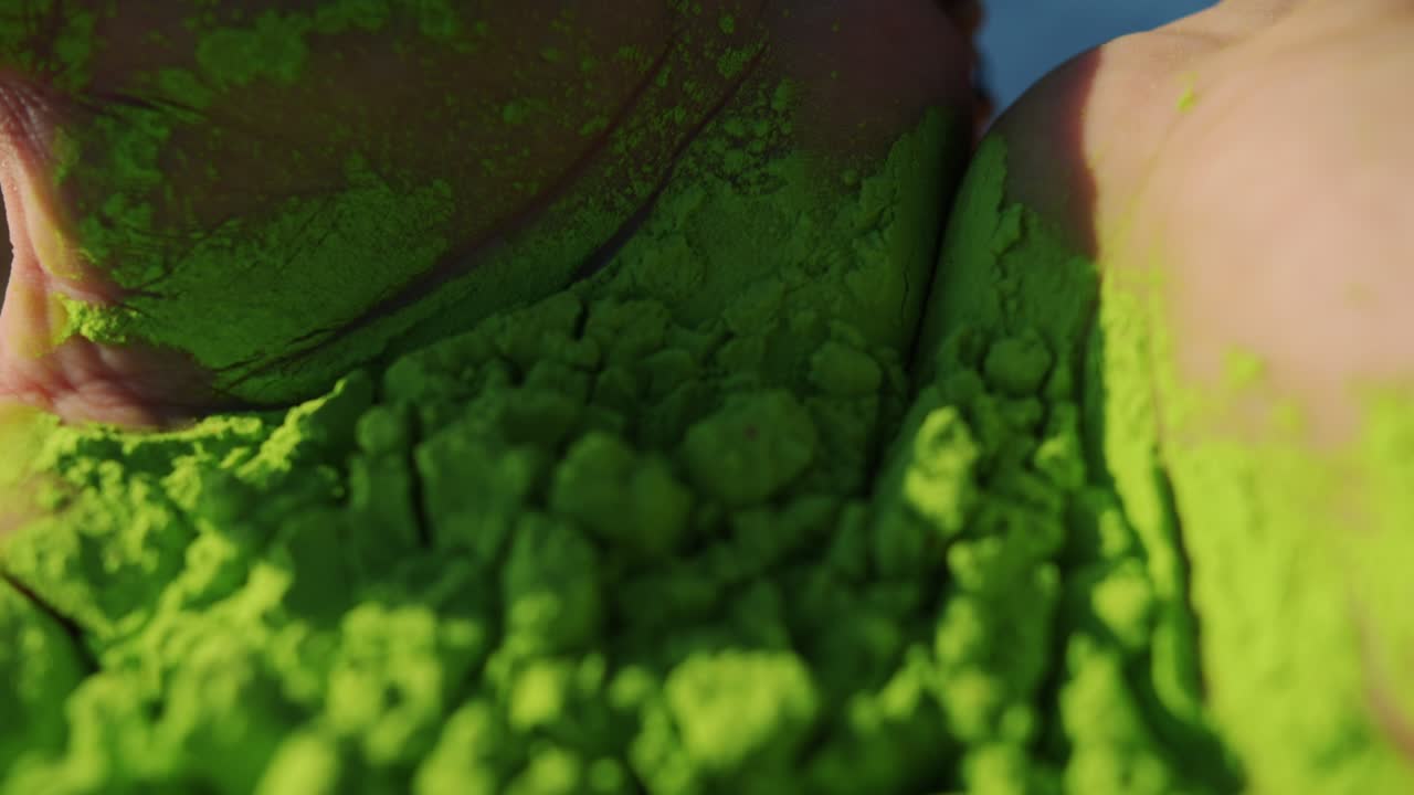 Nærbillede af håndflader fyldt med grønt farvet pulver, mens en person fejrer Holi-festivalen.