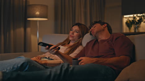 relaxed couple switching channels at home sofa evening. spouses choosing movie