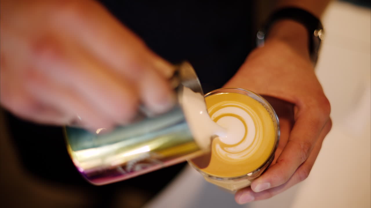 Close up of a barista pouring steamed milk into a glass of coffee