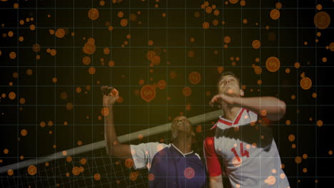 two male athletes jumping near goalpost in soccer match at night, showing orange confetti sparks