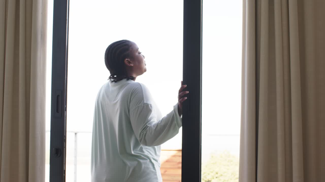 Holding door frame, woman is sliding glass door open and stepping onto balcony for viewing outdoors