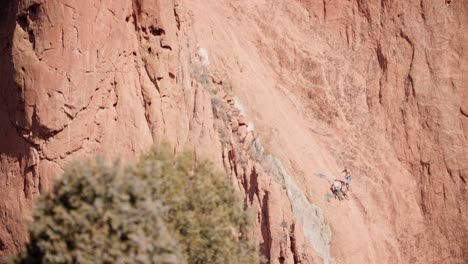 Climbers-ascending-the-red-rocky-face-at-Garden-of-the-Gods,-Colorado,-under-clear-skies