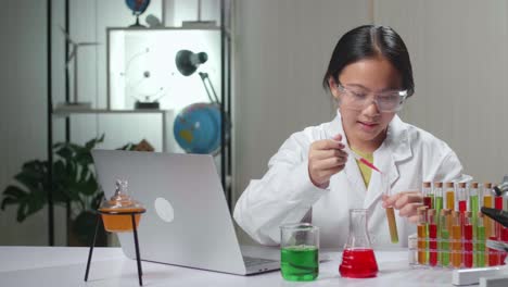 young asian scientist girl mixes chemicals in test tube and work with laptop computer. child learn with interest