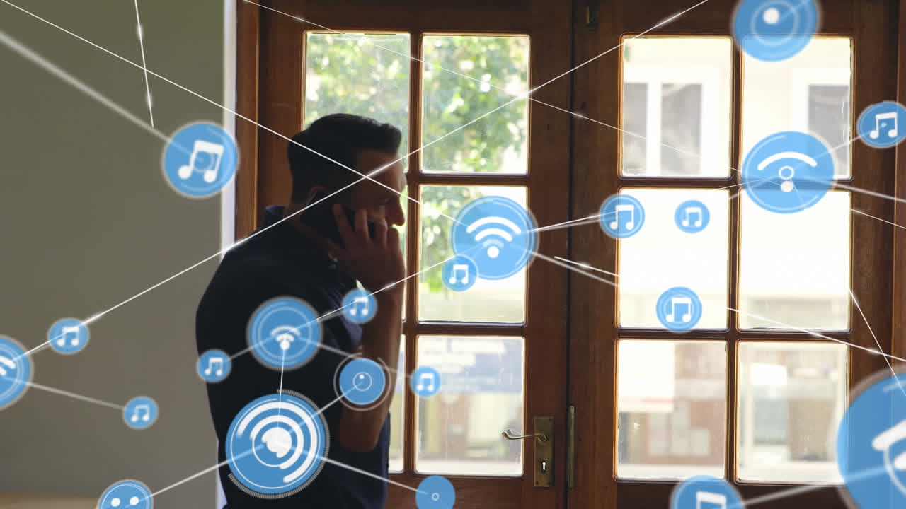 Network of digital icons against caucasian man talking on smartphone near the window at home