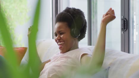 Happy-african-american-woman-wearing-headphones-sitting-on-sofa