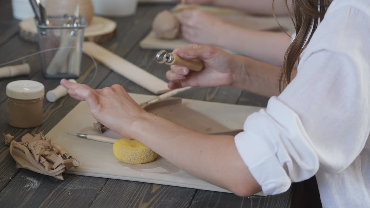 женщина, работающая с глиной руками и инструментом для резки петли, близко к керамической мастерской