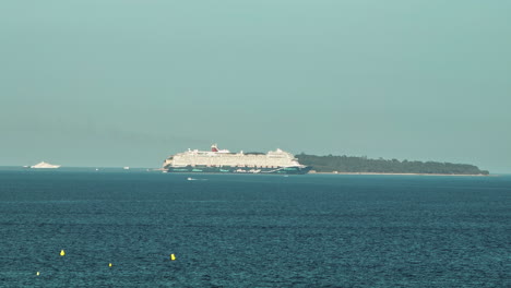 cruise ship sails past sainte marguerite, cannes backdrop.