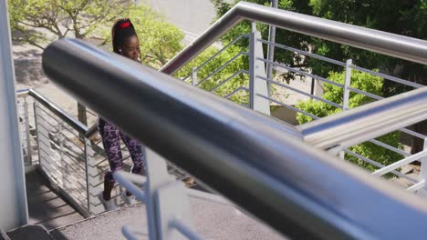 african american woman wearing earphones climbing up the stairs of the city bridge