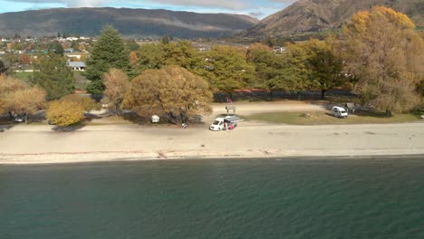 slowmo aerial drone ascending from the beach overviewing the town and lake wanaka, new zealand in autumn