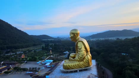 4k-360-Rundum-Drohnenaufnahmen-Einer-Riesigen-Goldenen-Mönchsstatue,-Umgeben-Von-Bergen-Von-Khao-Yai-In-Der-Abenddämmerung-In-Thailand