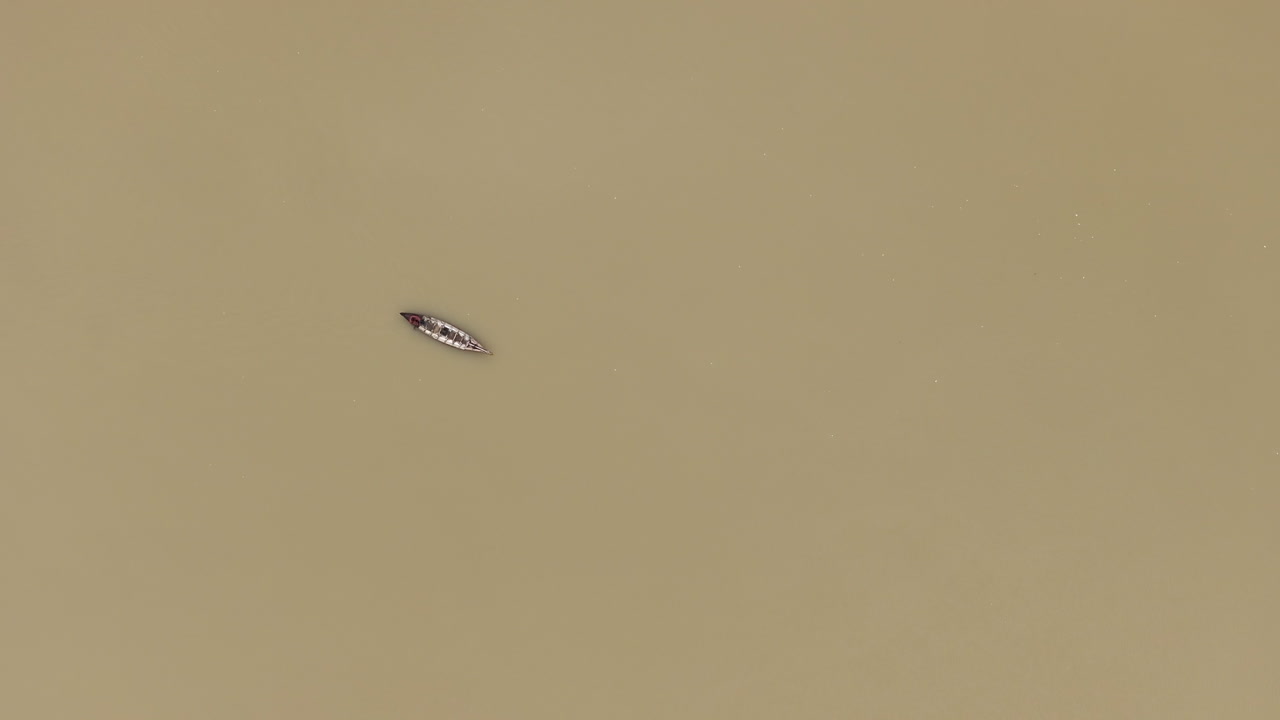 Aerial view of a small boat crossing vast muddy river waters in Cambodia