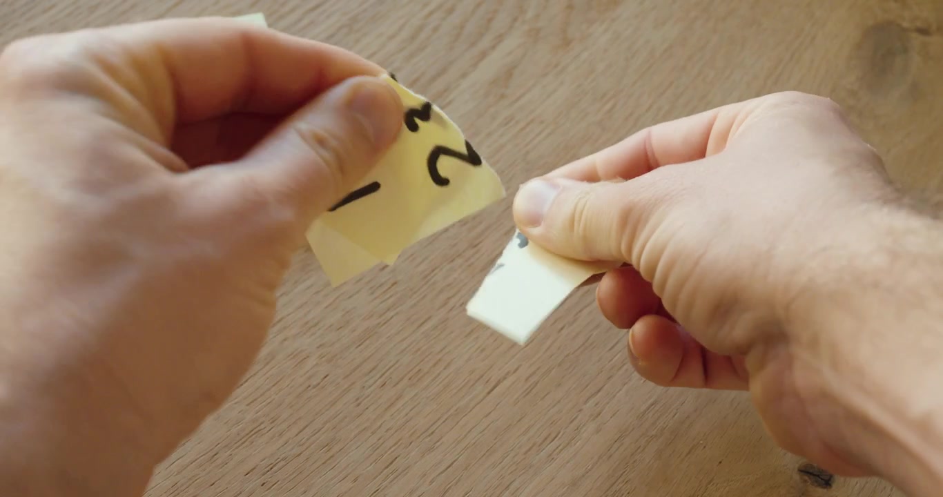 Close-up of hands tearing up a paper note with a handwritten PIN code, symbolizing IT security risk, data protection, privacy awareness, and safe handling of confidential information.