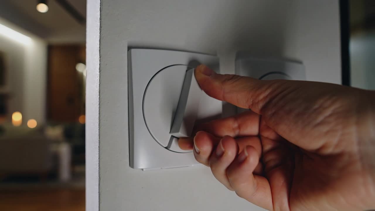 Reaching adult hand rotating dimmer lever on white wall in living room, changing lamps and candles