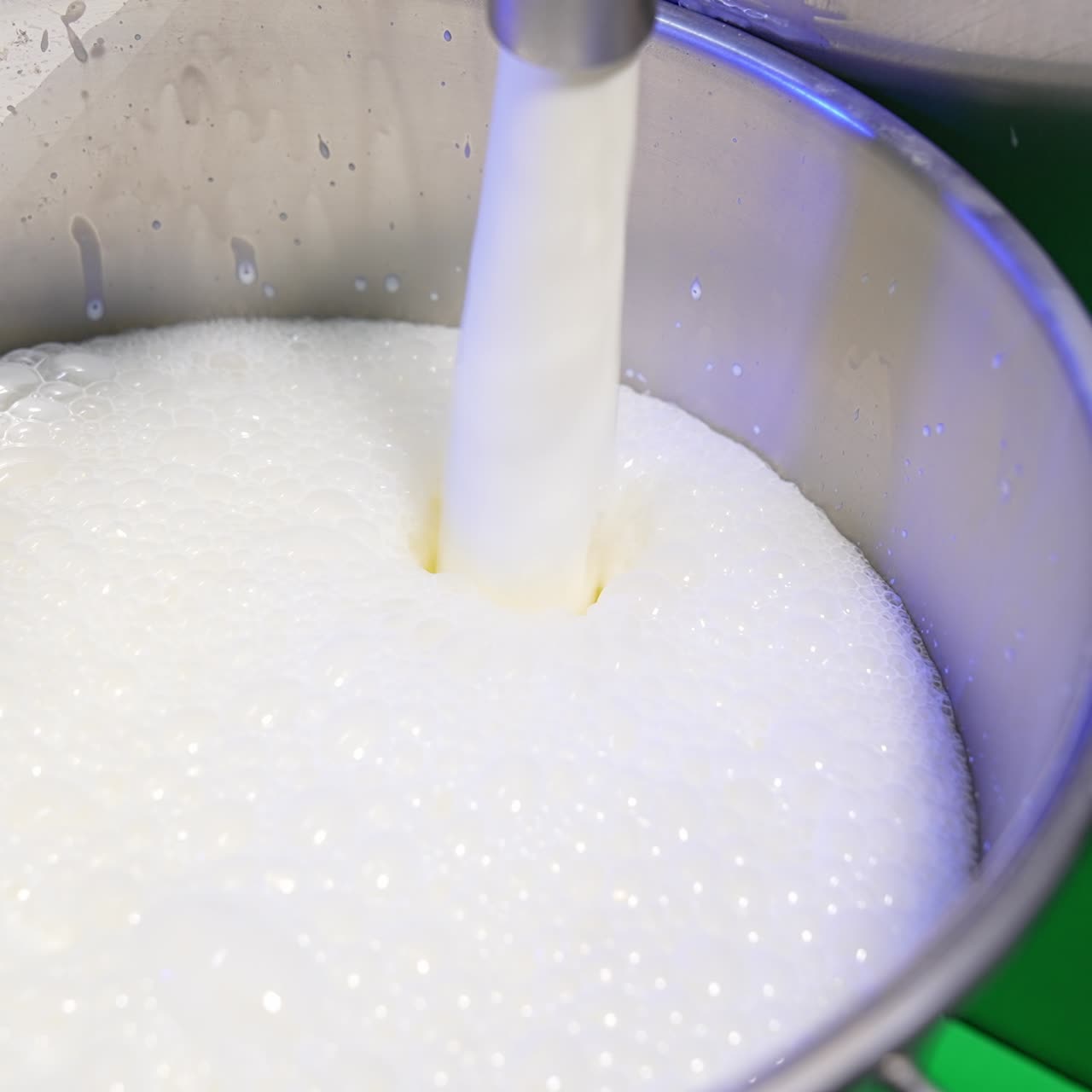 Fresh milk is pouring into a metal bucket creating foam on top. Close up. Food factory production concept
