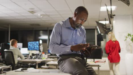 Thoughtful-professional-businessman-using-a-digital-tablet-while-sitting-on-his-desk-in-modern-offic