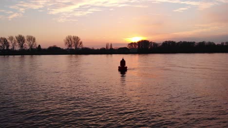 aerial silhouette of floating buoy in river during against orange sunset skies