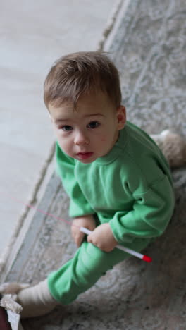 adorable baby boy sitting on the floor looking up with surprise. lovely toddler holding the toy for a cat. vertical video