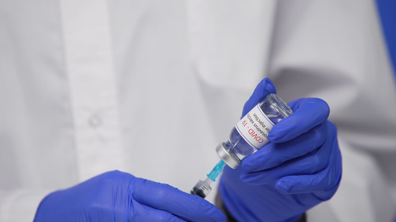 médico masculino sostiene la jeringa y la botella de la vacuna contra el coronavirus covid-19, concepto de tratamiento del virus corona y concepto de atención médica. pantalla azul, llave de croma. acercamiento. cámara lenta