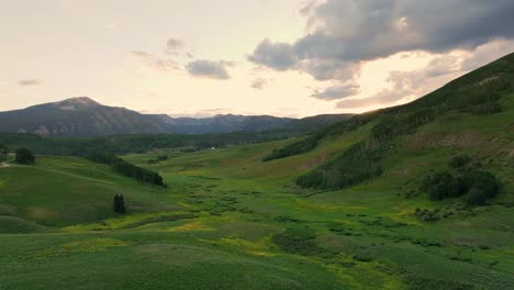 Aerial-at-sunset-over-a-lush-green-valley-near-Crested-Butte-mountain,-Colorado,-USA