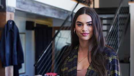 portrait of smiling female owner of fashion store standing in front of clothing display