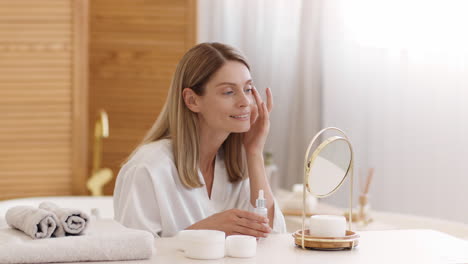 woman applying face serum as part of her daily skincare routine in the bathroom