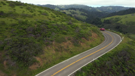 Sobrevuelo-Aéreo-De-La-Cresta-Con-Un-Camino-Muy-Ventoso-Debajo-Con-Tráfico-Constante-Y-Una-Vista-épica-De-Las-Montañas-Del-Norte-De-California-En-El-Fondo