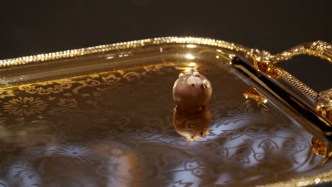 Hand-With-Plastic-Gloves-Placing-Chocolates-And-Date-On-A-Gold-Tray---close-up