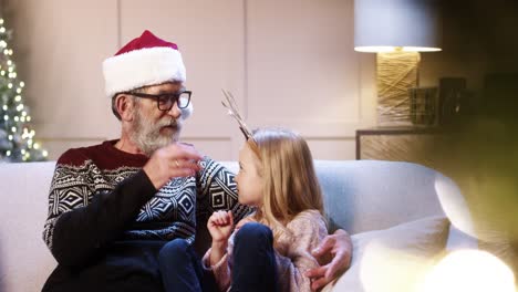 Nahaufnahme-Porträt-Einer-Glücklichen-Familie-Alter-Großvater-Mit-Süßer-Kleiner-Enkelin,-Die-In-Einem-Dekorierten-Raum-In-Der-Nähe-Des-Weihnachtsbaums-Sitzt-Und-Silvester-Zusammen-Verbringt-Und-Spricht