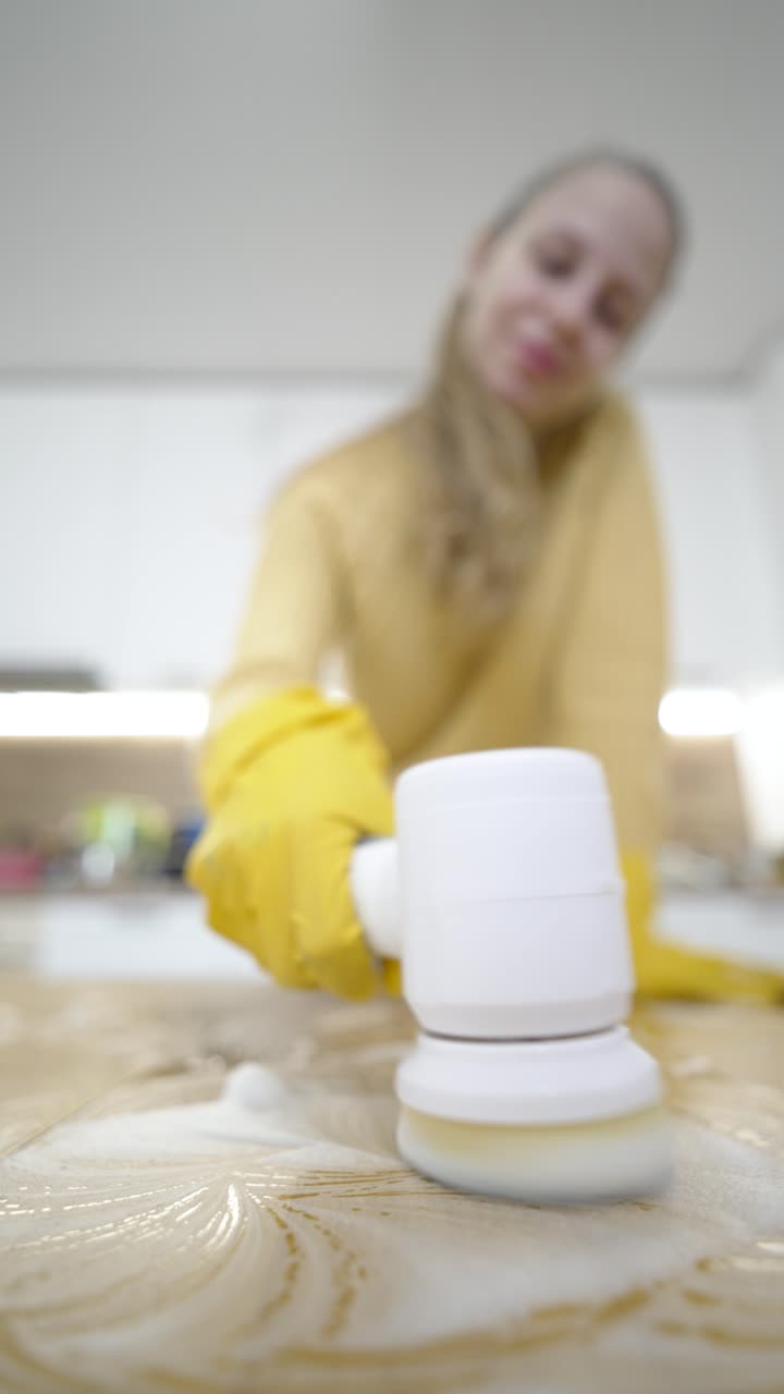 Video verticale mostra una donna che pulisce un tavolo con uno strumento elettrico, concentrandosi sulla pulizia profonda, la cura della casa e il mantenimento di un ambiente domestico pulito