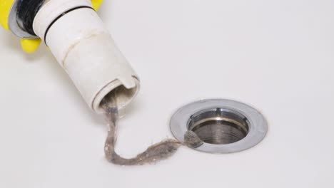 the water drain in the bathtub is clogged with hair. the water drain in the bathtub is clogged with hair. a plumber’s hand cleans clogs and removes hair. the concept of flushing water drain pipes