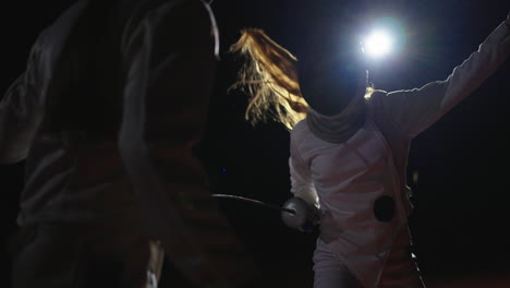 two fencers compete in a match, one in the foreground and one in the background.