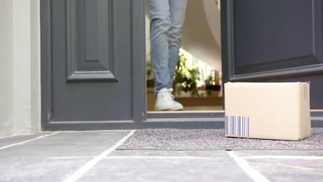 Low-section-of-biracial-man-picking-up-cardboard-box-outside-front-door,-copy-space,-slow-motion