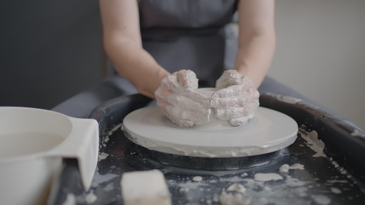 Elderly woman master works on a potter's wheel and makes a mug of ceramics in her workshop in slow motion