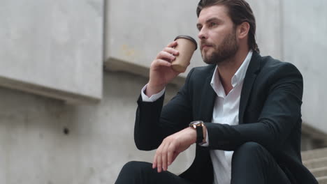 Businessman-drinking-take-away-coffee-in-city.-Male-worker-sitting-on-stairs