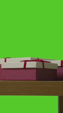 vertical video of presents in gift wrapped boxes on table shot against green screen 1