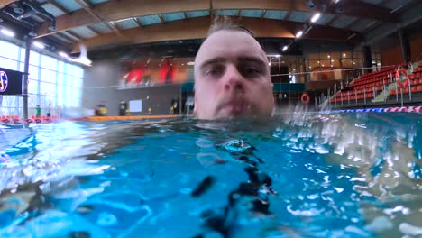 man swimming and diving at indoor pool while facing the camera