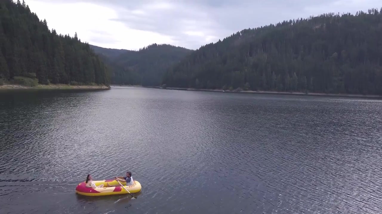 Due persone navigano su una zattera gialla attraverso un lago tranquillo circondato da colline boscose. Ideale per temi di esplorazione e natura. Perfetto per contenuti di viaggio.