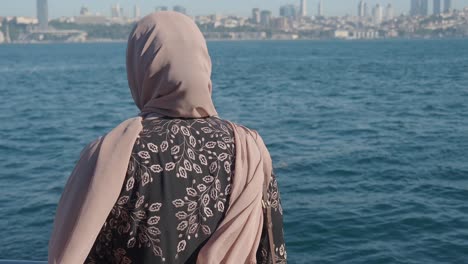 woman in hijab looking at a city skyline over the water