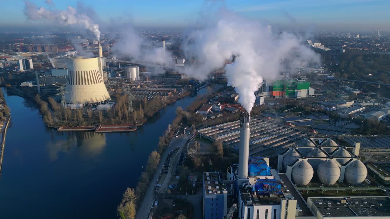 industrial heating plant with chimney releasing smoke into blue sky, impacting environment by a canal. Wonderful aerial view panorama overview static tripod hovering drone