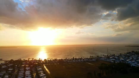 A-pretty-drone-shot-of-a-cloudy-sunset-going-down-with-houses-and-buildings-near-by-in-a-tropical-Florida-day-with-water-near-by