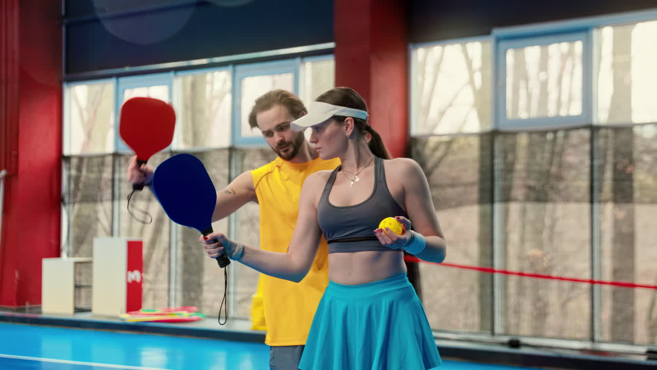 A man teaching a woman how to play pickleball in an inside court