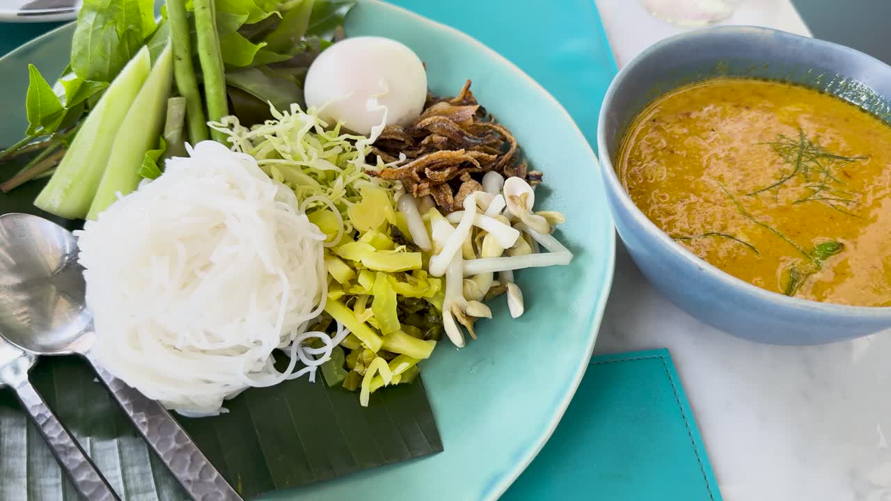 A vibrant display of Kanom Jeen Nam Ya Pu, showcasing fresh ingredients and rich curry sauce in a bright, inviting setting