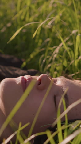 primo piano di una giovane donna sdraiata in un campo erboso illuminato dal sole, perduta nei suoi pensieri, circondata da un'alta erba verde che incornicia dolcemente il suo viso, il caldo bagliore della luce solare sullo sfondo