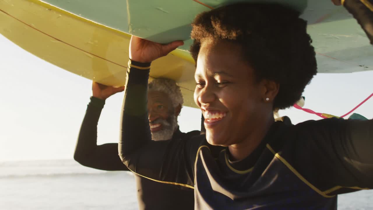 Happy african american couple walking with surfboards on sunny beach