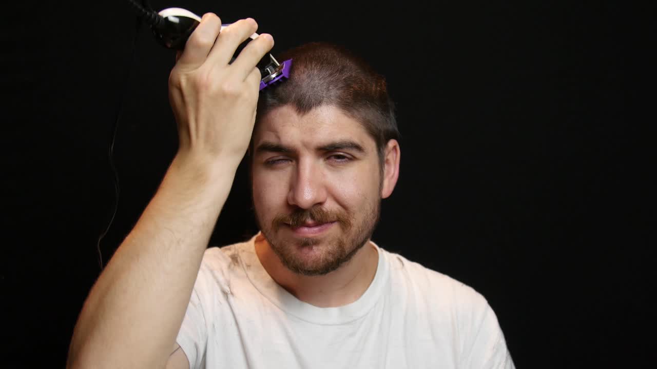 Uomo che si guarda allo specchio mentre si taglia i capelli a macchinetta.